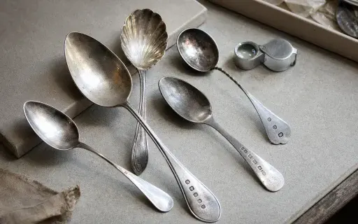 Old spoons on a work surface with a magnifying loupe for mark inspection.